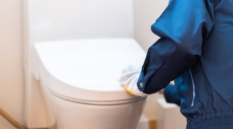 手袋をした職人が新しい便器を据え付けて位置を調整する手元